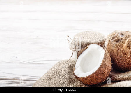Guscio di noce di cocco con la carne sulla canapa sacco su legno bianco tavolo da cucina Foto Stock