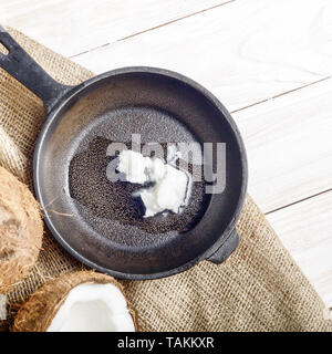 Noce di cocco, shell con carne, padella in ghisa sulla canapa sacco su legno bianco tavolo da cucina Foto Stock
