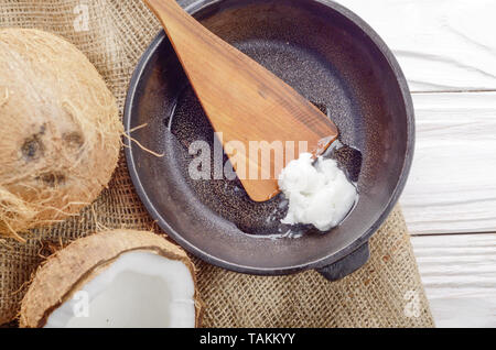 Noce di cocco, shell con carne, padella in ghisa e la spatola sulla canapa sacco su legno bianco tavolo da cucina Foto Stock