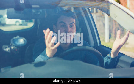 Arrabbiato uomo alla guida di un veicolo sostenendo e gesticolando scuotendo le sue mani perplesso. Irritato e furiosa conducente guy negativo espressione facciale, seduto in Foto Stock