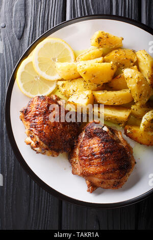 Tradizionale greco aglio limone patate arrosto (Patates fournou) con grigliate di cosce di pollo su una piastra vicino sul tavolo. Verticale in alto visualizza fro Foto Stock