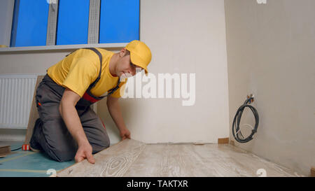 Giovani tuttofare l'installazione di un pavimento in legno nella nuova casa. Lavoratore mette il bordo della pavimentazione. Home Concetto di riparazione. Foto Stock