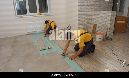 Costruttori installazione pavimento in laminato. Lavoratori qualificati lay pavimenti in laminato. Costruzione e ristrutturazione di casa. Foto Stock