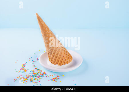 Gelato alla vaniglia sulla piastra bianca con disegno waffle coni e caramelle colorate su sfondo blu Foto Stock