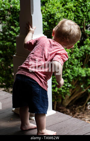 A piedi nudi toddler maschio coetanei di tutto il post sulla veranda in legno. Foto Stock
