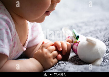 Piccolo Bambino tiene in mano il suo giocattolo preferito un sonaglio infanzia felice Baby Unfocused come sfondo Foto Stock