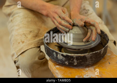 Lo stampaggio di pentola di fresco. Uomo forte con le mani sporche di seduta in legno sulla ruota della ceramica e la produzione di nuova creazione Foto Stock