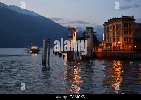 Varenna/Italia- Aprile 6, 2014: bella vista panoramica verso il lago di Como con una nave passeggeri allontanandosi dalla porta di Varenna al tramonto in primavera. Foto Stock