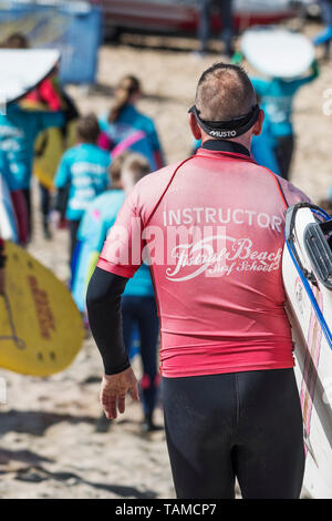 Un istruttore di surf con il Fistral Beach Surf School l'impostazione Off per eseguire una lezione di surf a Newquay in Cornovaglia. Foto Stock