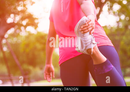 Sport donna stretching muscolare delle gambe la preparazione per la corsa nel parco pubblico all'aperto. Close up di atleta femminile della parte inferiore del corpo facendo gambe distese getting Foto Stock