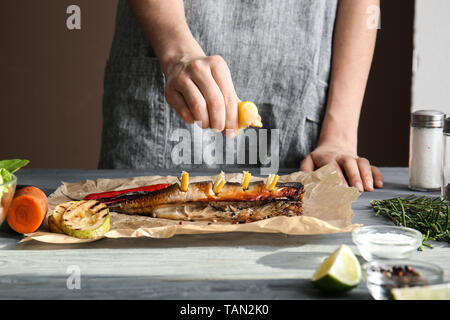 Donna spremendo il succo di limone su gustoso pesce sgombro su tavola Foto Stock