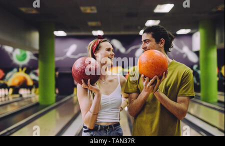 Allegro coppia giovane al bowling con le sfere guardando ogni altro. Giovane uomo e donna in piedi in un bowling club le sfere di trattenimento. Foto Stock