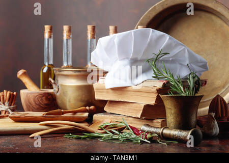 Chef di Bianca Cappello e vecchi libri di cucina. Utensili da cucina con spezie e rosmarino su una vecchia tabella marrone. Foto Stock