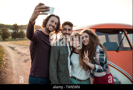 Un gruppo di giovani amici su roadtrip attraverso la campagna, tenendo selfie. Foto Stock