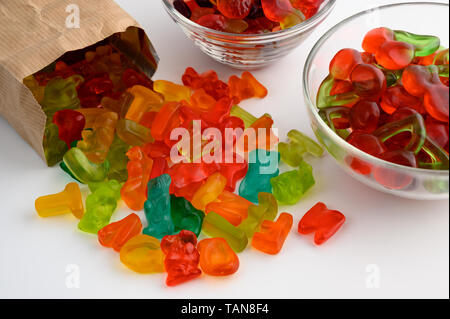 Ciotole in vetro e sacchetto di carta colorata di caramelle gommose su sfondo bianco Foto Stock