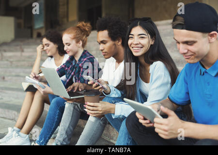 Multietnica diversi amici utilizzando dispositivi digitali all'aperto Foto Stock