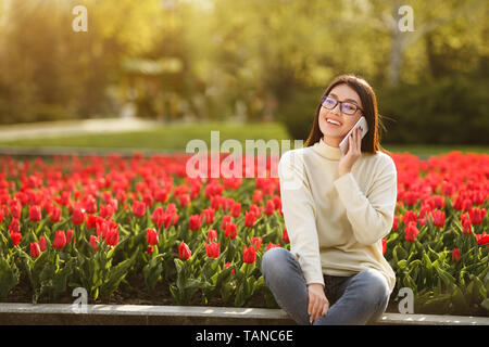 Ragazza dello studente in appoggio nel parco e parlando al telefono Foto Stock