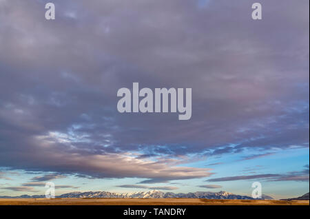 Vista panoramica di una maestosa catena montuosa ricoperta con sharp bianco della neve. Azzurro cielo quasi riempito con spesse nuvole grigio può essere visto attraverso la rete lan Foto Stock