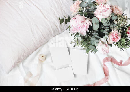 Accogliente camera da letto ancora vita scena. Matrimoni, compleanni bouquet di rose rosa peonia, fiori e rami di eucalipto. Nastri di seta su lino Biancheria da letto. Vuoto Foto Stock