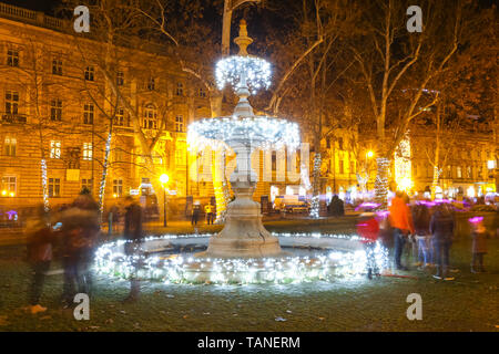 Il tempo di avvento nel centro della città di Zagreb, Croazia. La fontana illuminata in ornato parco Zrinjevac con sfocata persone intorno ad esso. Foto Stock
