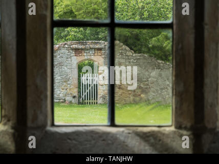 Un cancello in una parete, visto da una finestra di vetro antico al Cleeve Abbey, Somerset Foto Stock