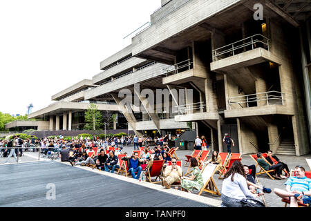 Le persone sedute a sdraio nella Southbank davanti al National Theatre di Londra, Regno Unito Foto Stock