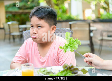 Obesi Fat Boy con espressione di disgusto contro le verdure in insalata, rifiutando il concetto di cibo Foto Stock