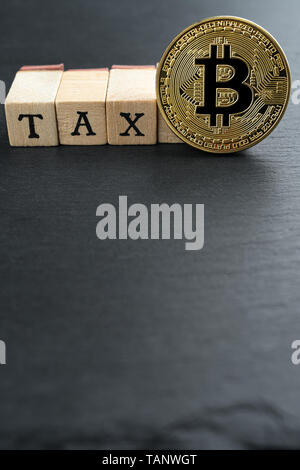 Bitcoin fisico moneta in oro con testo fiscali realizzate in blocchi di legno su pietra scura piastra di ardesia sfondo. Tassazione Cryptocurrency concetto astratto. Cop Foto Stock