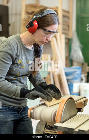 Giovane donna usando una levigatrice a nastro alla sabbia tavolato in legno in officina Foto Stock