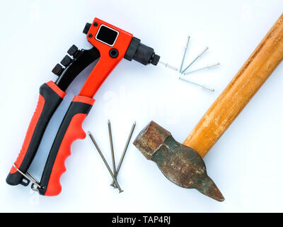 Un vecchio martello con un manico di legno e un mucchio di chiodi contro la nuova pistola rivettatrice e un mazzetto di rivetti Foto Stock