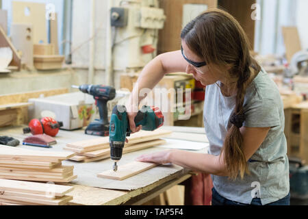 Giovane donna con trapano effettuare il foro in asse in legno in officina Foto Stock