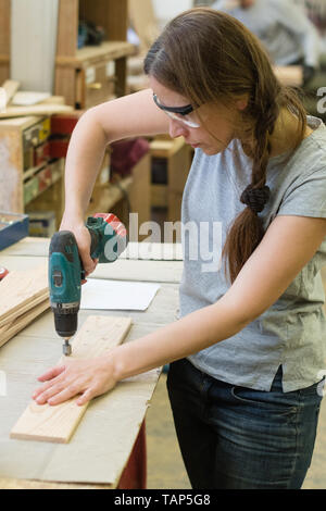 Giovane donna con trapano effettuare il foro in asse in legno in officina Foto Stock