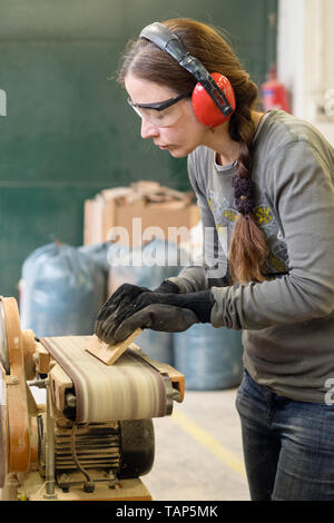 Giovane donna usando una levigatrice a nastro alla sabbia tavolato in legno in officina Foto Stock