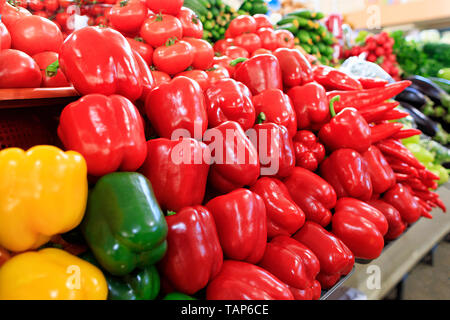 Diverse varietà di rosso, giallo e peperoni verdi in background in sfocata cetrioli, spinaci e altri ortaggi sono venduti in vaschette sulla Foto Stock