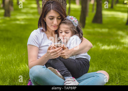 Giovane mamma e bambina guardare foto a smart phone dopo prendere selfie.Felice madre e figlia momenti con amore e commozione naturale. Foto Stock