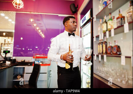 African American barista presso il bar tenendo con una bottiglia di champagne e bicchieri. Foto Stock