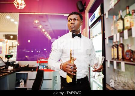 African American barista presso il bar tenendo con una bottiglia di champagne e bicchieri. Foto Stock