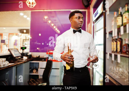 African American barista presso il bar tenendo con una bottiglia di champagne e bicchieri. Foto Stock