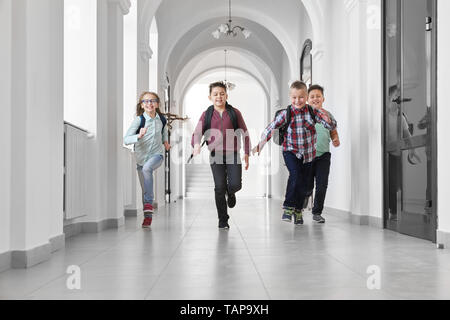 Gruppo di felice, positivo scolari in esecuzione nel lungo corridoio della scuola. Ragazzi e una ragazza ridere, nella pausa tra le lezioni. I compagni di scuola sorridente e in esecuzione. Foto Stock