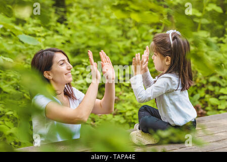 Giovane mamma e la sua bambina divertirsi insieme sulla panca di legno nella foresta.Felice madre e figlia momenti con amore e commozione naturale Foto Stock