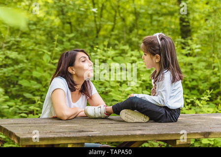 Giovane mamma e la sua bambina divertirsi insieme sulla panca di legno nella foresta.Felice madre e figlia momenti con amore e commozione naturale Foto Stock