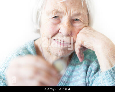 Allegra anziana donna di 96 anni seduta a tavola a casa felice con una moneta in mano. Risparmio per pensionamento e pianificazione finanziaria concetto Foto Stock