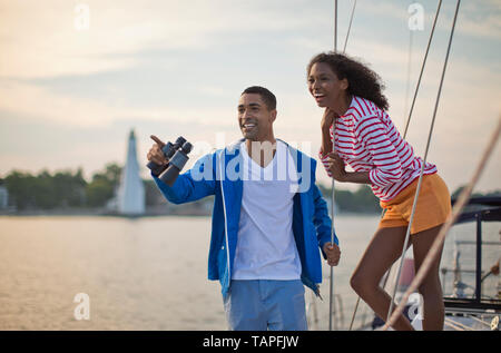 Felice coppia giovane divertendosi con un binocolo mentre la vela. Foto Stock
