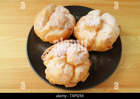 Piastra di tre francesi bignè o Choux a la Creme Dolci serviti sulla tavola di legno Foto Stock