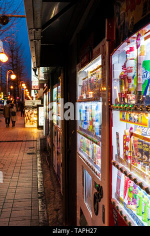 Vista lungo la fila di giapponese di soft drink distributori automatici sulla strada di notte tempo nella città di Kumamoto, Giappone. Foto Stock