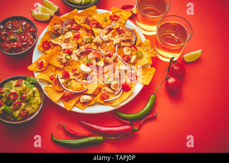 Una piastra di deliziose tortillas nachos con formaggio fuso e salsa di pollo alla griglia, i peperoncini jalapeno, cipolla rossa, pomodoro, guacamole dip e salsa piccante. Wi Foto Stock