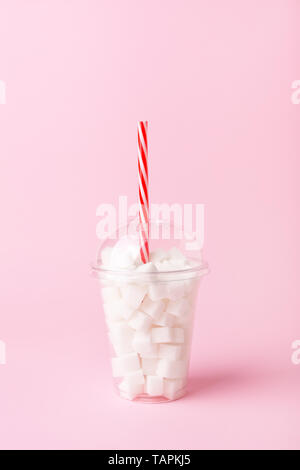 Agitare in plastica vetro con paglia pieno di cubetti di zucchero sul rosa pastello sfondo. Una dieta poco sana nozione. Il minimo, verticale, vista laterale. Foto Stock