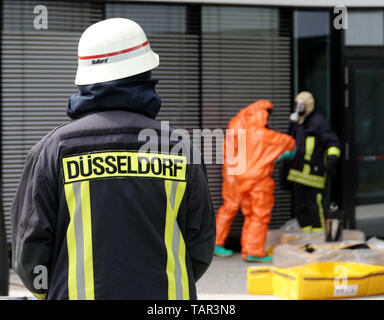 Duesseldorf, Germania. 27 Maggio, 2019. Un vigile del fuoco guarda i vigili del fuoco del Düsseldorf vigili del fuoco di entrare in un edificio per uffici presso l'aeroporto di Düsseldorf in tute di protezione. A causa di uno sconosciuto polvere bianca in costruzione, il dipartimento dei vigili del fuoco è andato su una operazione su larga scala. Credito: Johannes Neudecker/dpa/Alamy Live News Foto Stock