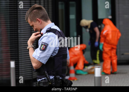 Duesseldorf, Germania. 27 Maggio, 2019. Un poliziotto radioing è un edificio di uffici presso l'aeroporto di Düsseldorf mentre dietro di lui i vigili del fuoco da Düsseldorf vigili del fuoco in tute di protezione sono di entrare. A causa di uno sconosciuto polvere bianca in costruzione, i vigili del fuoco è andato su una operazione su larga scala. Credito: Johannes Neudecker/dpa/Alamy Live News Foto Stock