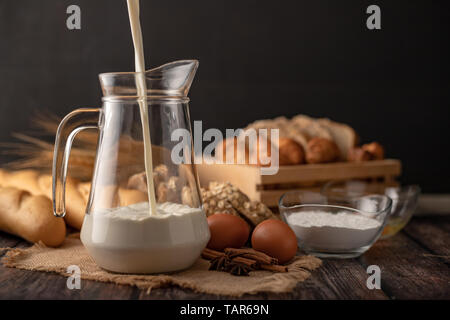 Versare il latte in un recipiente posto sul sacco. Un sacco di pane e uova giacciono su di un tavolo di legno. Foto Stock